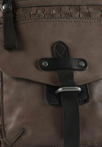 Bruine leren tas met een getextureerde klep, zwarte riem en zilverkleurige hardware. Heeft een gestikte detail langs de bovenkant en een leren sluiting.