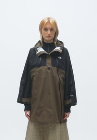 Brūna un melna ūdensizturīga jaka ar kapuci, ar rāvējslēdzējiem, regulējamām piedurknēm un elpojošu dizainu. Gluda tekstūra un funkcionālas kabatas.