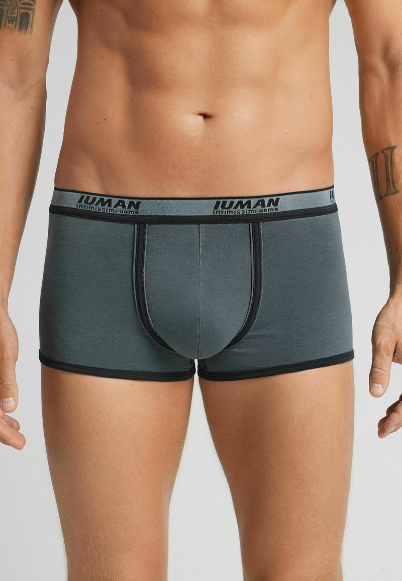 Grå boxershorts med svart midjeband som har varumärkesnamnet. Slät textur, figursydd design och korta ben med kontrasterande trim.