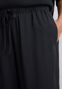 Zwarte, lichte broek met een elastische tailleband, een trekkoorddetail en zijzakken; gladde textuur en een relaxte pasvorm.