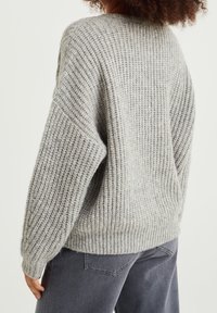 Grau gestrickter Pullover mit lockerem Sitz, strukturierter Rippung und überschnittenen Schultern. Hergestellt aus weichem Material mit einer leicht übergroßen Silhouette.