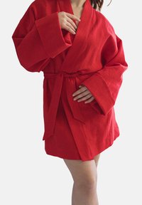 Czerwona lniana szata z szerokimi rękawami i paskiem, charakteryzująca się teksturowanym splotem i długością do kolan. Prosty design, bez wzorów ani akcentów.