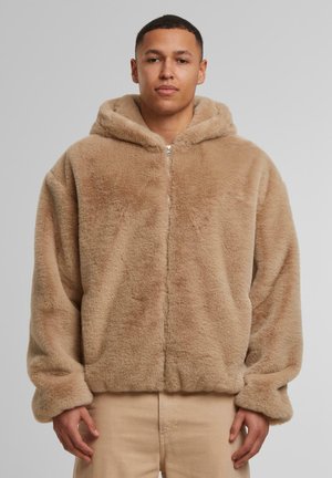 Beige faux fur hooded jacket with a zip front, featuring a soft texture, relaxed fit, and oversized sleeves.