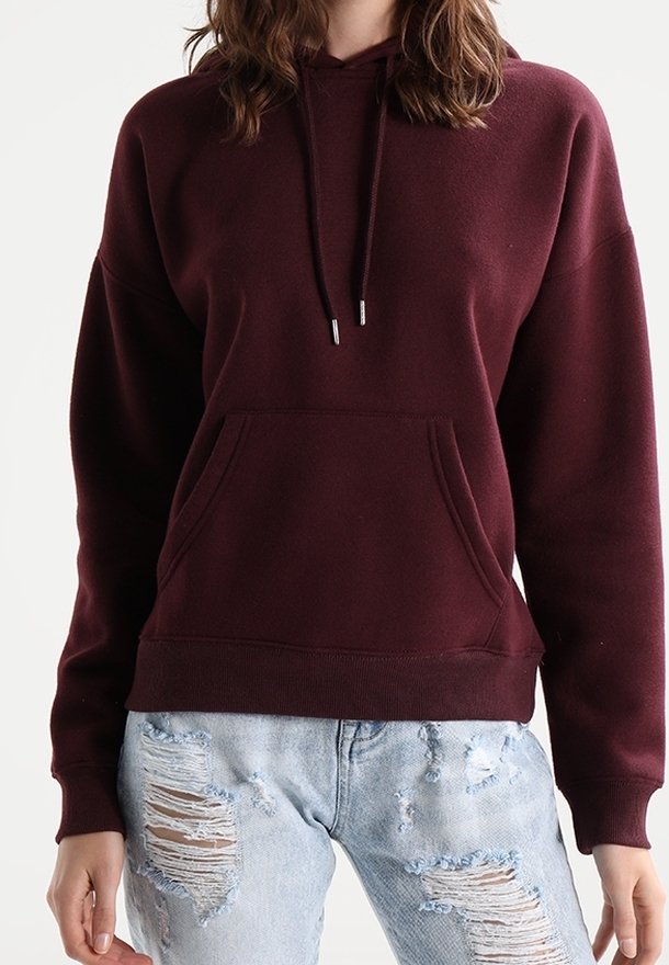 Sudadera burdeos con bolsillo frontal, capucha con cordón y puños acanalados. Combinada con jeans claros desgastados.