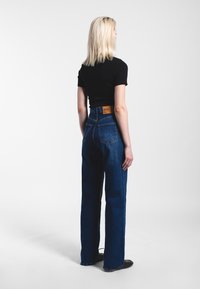 High-waisted blue jeans made of denim, featuring a rear patch pocket and a tan leather label on the waistband. Loose, straight-leg cut.