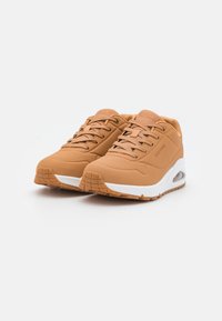 Braune Sneakers mit glattem Obermaterial, Mesh-Details, gepolsterter Sohle, weißer Zwischensohle und strukturiertem Gummiaußensohle. Schnürsenkel und Branding in passender Farbe.
