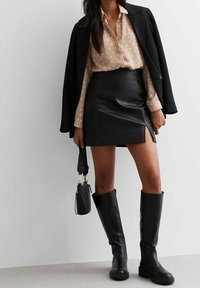 Svart läder mini kjol med en sidofåra, kombinerad med en beige prickig skjorta och en svart blazer. Svarta knähöga stövlar fulländar looken.