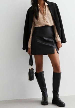 Czarna skórzana mini spódnica z bocznym rozcięciem, w połączeniu z beżową koszulą w kropki i czarnym żakietem. Całość dopełniają czarne kozaki za kolano.