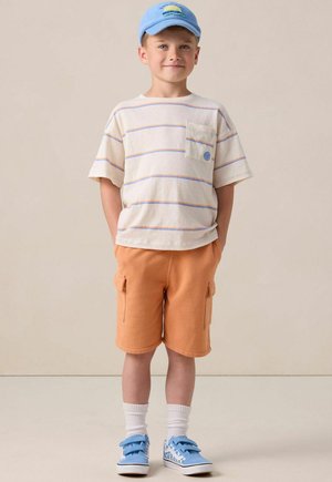 Enfant portant une chemise à manches courtes rayée crème et bleue, un short cargo orange, des baskets bleues avec un motif à carreaux blancs, et une casquette bleue.