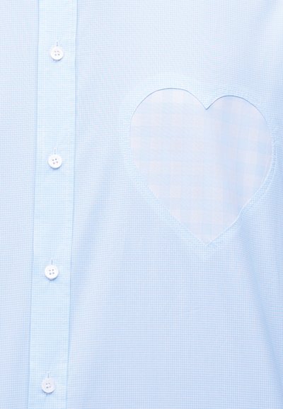 Ανοιχτό μπλε πουκάμισο με κουμπιά, με μια καρδιόσχημη πατζήτα στο στήθος σε λίγο πιο σκούρα μπλε καρό μοτίβο.