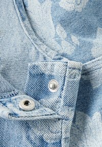Svijetloplava denim tkanina s cvjetnim uzorkom, s metalnim srebrnim kopčanjem i detaljnim šavovima duž rubova.