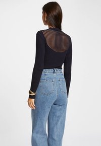 Haut noir à manches longues côtelées avec un dos en voile rayé, associé à un jean en denim bleu taille haute avec poches arrière et une coupe décontractée.