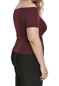 Burgundy off-shoulder topp med korta ärmar, ribbat mönster, figurnära design och rak nederkant, matchad med svarta byxor.