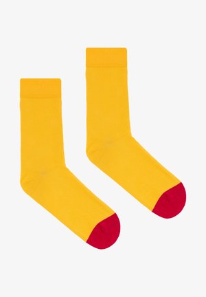 Żółte bawełniane skarpetki o jednolitym wzorze, z czerwonymi palcami. Gładka tekstura, długość do połowy łydki i prążkowane wykończenie na górze zapewniające pewne dopasowanie.