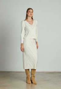 Robe blanche à motif avec un décolleté en V et des manches longues, présentant des motifs en zigzag. Assortie à des bottes marron à hauteur de genoux. Texture lisse.