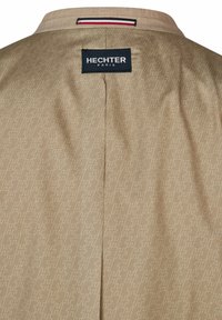 Chemise beige avec motif géométrique, arborant une étiquette noire HECHTER Paris au dos. Texture lisse avec un léger éclat.