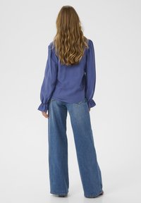 Purple long-sleeve blouse with puffed shoulders, paired with wide-leg blue denim jeans. Smooth texture, simple design, and relaxed fit.