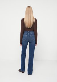 Jeans de mezclilla azul de talle alto con un diseño de pata recta, que cuentan con bolsillos traseros y una textura ligeramente desgastada.