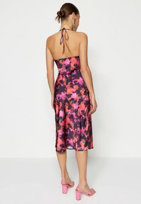 Bardotklänning i flerfärgad blommönster med satinfinish; mjuk textur, midilängd, baksidig knytning, bärs med rosa klacksandaler.