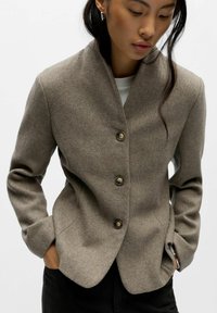 Bruine, gestructureerde blazer met sjaalkraag en sluiting met vijf knopen, voorzien van twee zijzakken en een getailleerde pasvorm.