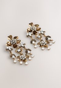 Gold-tone floral earrings with intricate detailing, featuring clear rhinestones and dangling pear-shaped accents. Leafy embellishments present.