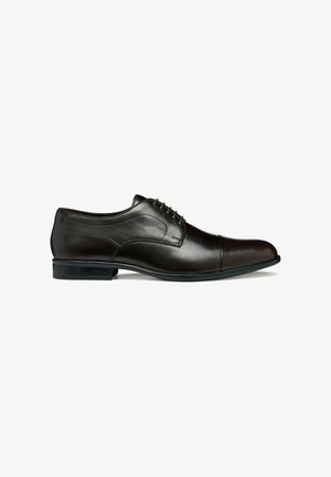 Zapato Oxford de cuero negro para hombre con cierre cerrado, detalle de puntera y tacón bajo sobre fondo blanco.