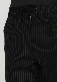 Svarta kostymbyxor med veck, tillverkade av ett lent tyg, med en elastisk midja och dragsko för justerbar passform.