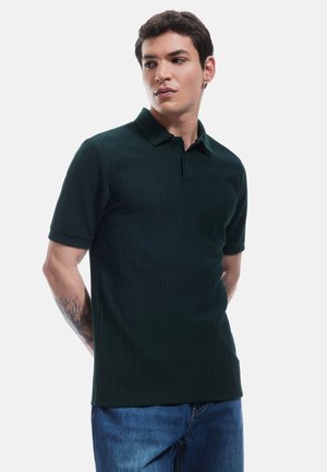 Mørkegrøn, ribbet polo-shirt med krave, korte ærmer og lige kant, parret med blå denim jeans.