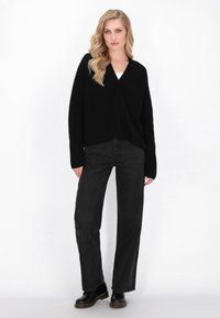 Cardigan avvolgente nero a coste con maniche lunghe, chiusura con un bottone e orlo corto, abbinato a pantaloni neri a gamba dritta a vita alta e stivali neri.