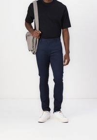 Marinblå slim-fit-byxor med raka ben, kombinerat med en svart t-shirt med kort ärm och vita sneakers; bär en ljusgrå axelväska.