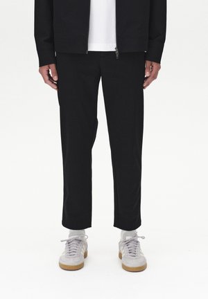 Black tapered pants paired with white crew socks and light gray sneakers. The fabric is smooth, with a relaxed fit and a cropped length.