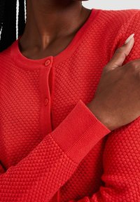 Cardigan rosso in maglia con un motivo testurizzato, scollo rotondo e chiusura con bottoni. Le maniche e l'orlo a costine arricchiscono il design.