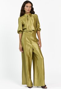 Olijfgroen twee-delig outfit met een strik-kraag, volumineuze korte mouwen en een wijde broek, gemaakt van een glanzende, textuurrijke stof.