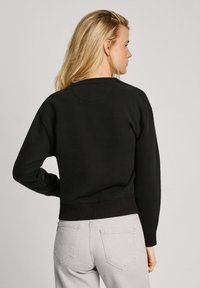 Sudadera negra con cuello redondo, puños y dobladillo de punto acanalado, y corte relajado. Acompañada de jeans gris claro en un estilo casual.