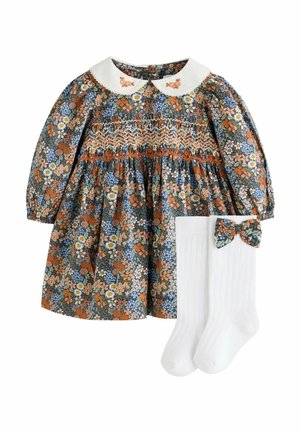 Kvetinové šaty s dlhým rukávom so smock detailmi a bielym golierom Peter Pan, doplnené bielymi podkolienkami s kvetinovou mašľou.