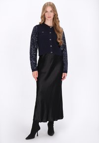 Tengerész kék, rövidített kardigán díszített ujjal, ezüst gombokkal, hosszú fekete selyem szoknyával és testhez álló fekete magassarkú csizmával párosítva.