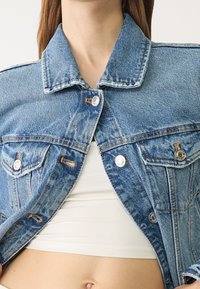 Jeansjacka i ljusblått, med klassisk krage, knäppning fram, två bröstfickor och synliga sömmar.