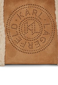 Materialul de suede bej prezintă un model circular de perforații cu textul "KARL" și stele, înconjurat de o textură moale de culoare crem.