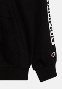 Felpa nera con stampa bianca "CHAMPION" lungo la manica. Presenta polsini e orlo a costine. Piccolo logo ricamato in rosso e bianco.