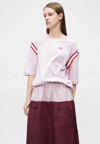Ροζ βαμβακερό t-shirt με κόκκινες ρίγες στα μανίκια και λογότυπο "BP". Φοριέται με μπορντό πολυεπίπεδη φούστα με τσέπες και διάφανο επικάλυμμα.