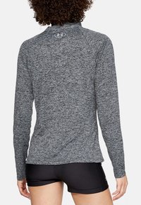 Maglietta sportiva a maniche lunghe in tessuto grigio melange, con colletto alto, texture a coste e logo sul retro, abbinata a pantaloni corti neri.
