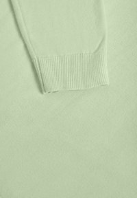 Manche de pull en maille vert clair avec poignet côtelé reposant sur un fond en tissu tricoté assorti.