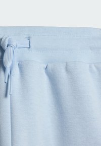 Svijetloplave trenirka hlače od teksturiranog tkanja, s elastičnim pojasom i podesivim vezicama. Ušiveni nabori dodaju volumen u području struka.