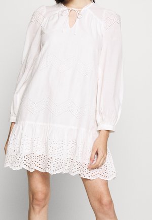 Biała sukienka z długim rękawem, z wycięciami w zygzakowaty wzór oraz brzegiem z koronki z oczkami, z wiązaniem przy dekolcie i luźnym, zwiewnym krojem.