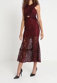 Burgundowa sukienka z koronką z dopasowaną górą, z wycięciem oraz zwiewną koronkową spódnicą z rozkloszowanym dołem. Połączona z czarnymi szpilkami.