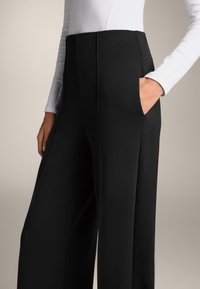 Fekete, bő szárú nadrág magas derékkal, oldalsó zsebekkel és sima textúrával. Egy illeszkedő, fehér, hosszú ujjú toppal párosítva.