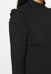 Schwarzes Langarmshirt mit Stehkragen, das über eine strukturierte Rippung und geraffte Schulterdetails verfügt und eine figurbetonte Silhouette bietet.