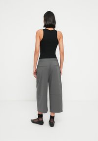 Μαύρο τοπ χωρίς μανίκια συνδυασμένο με γκρι παντελόνι φαρδιάς γραμμής. Το παντελόνι διαθέτει τσέπες, λεία υφή και διακριτικό καρό μοτίβο. Μαύρα μπαλαρίνες με διαφανείς κάλτσες.