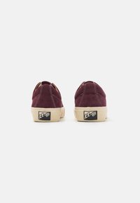 Burgundy suede sneakers with a low profile, beige rubber sole, contrasting stitching, and a black logo at the heel.