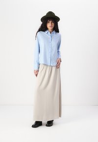 Blue and white striped button-up shirt paired with a beige maxi skirt, worn with black ankle boots and a dark green hat.